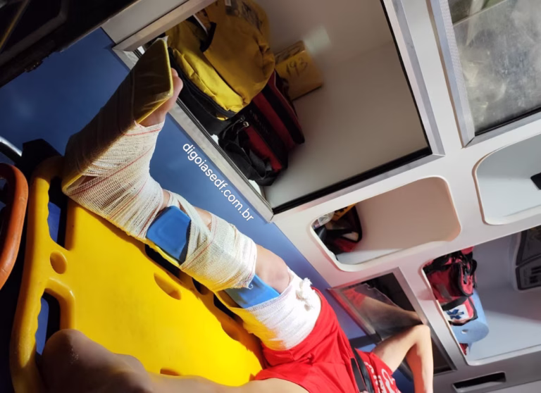 Jovem na maca dos bombeiros, com a perna imobilizada com tala e ataduras.