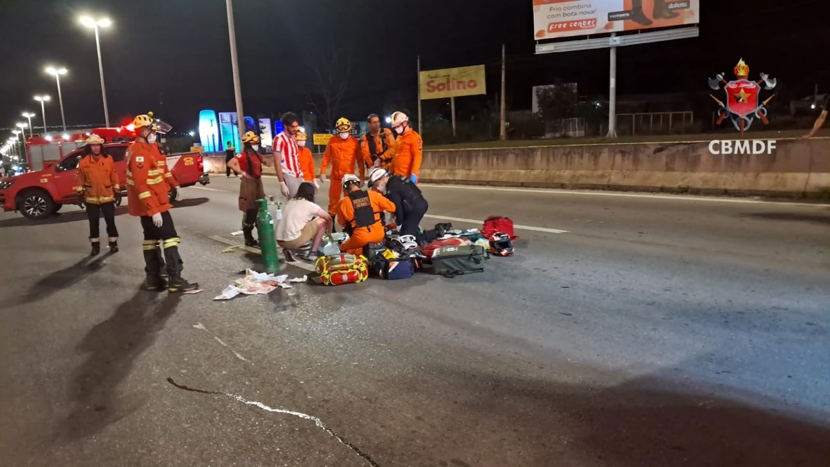 Equipes do Corpo de Bombeiros Militar do Distrito Federal realizam atendimento a um motociclista após acidente na marginal da BR-020, em frente ao Taquari, com viaturas de resgate e equipamentos de emergência posicionados na pista durante operação noturna.
