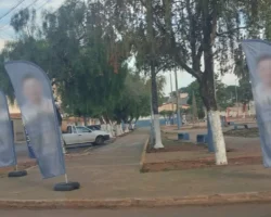 Bandeiras de propaganda eleitoral móvel instaladas ao longo de uma calçada pública, com rostos, nomes e números dos candidatos completamente desfocados e ilegíveis para preservação de identidade.