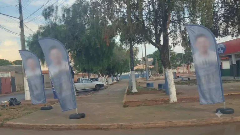 Bandeiras de propaganda eleitoral móvel instaladas ao longo de uma calçada pública, com rostos, nomes e números dos candidatos completamente desfocados e ilegíveis para preservação de identidade.